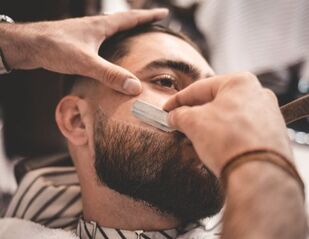 Man getting beard shaped in barbershop with straight razor